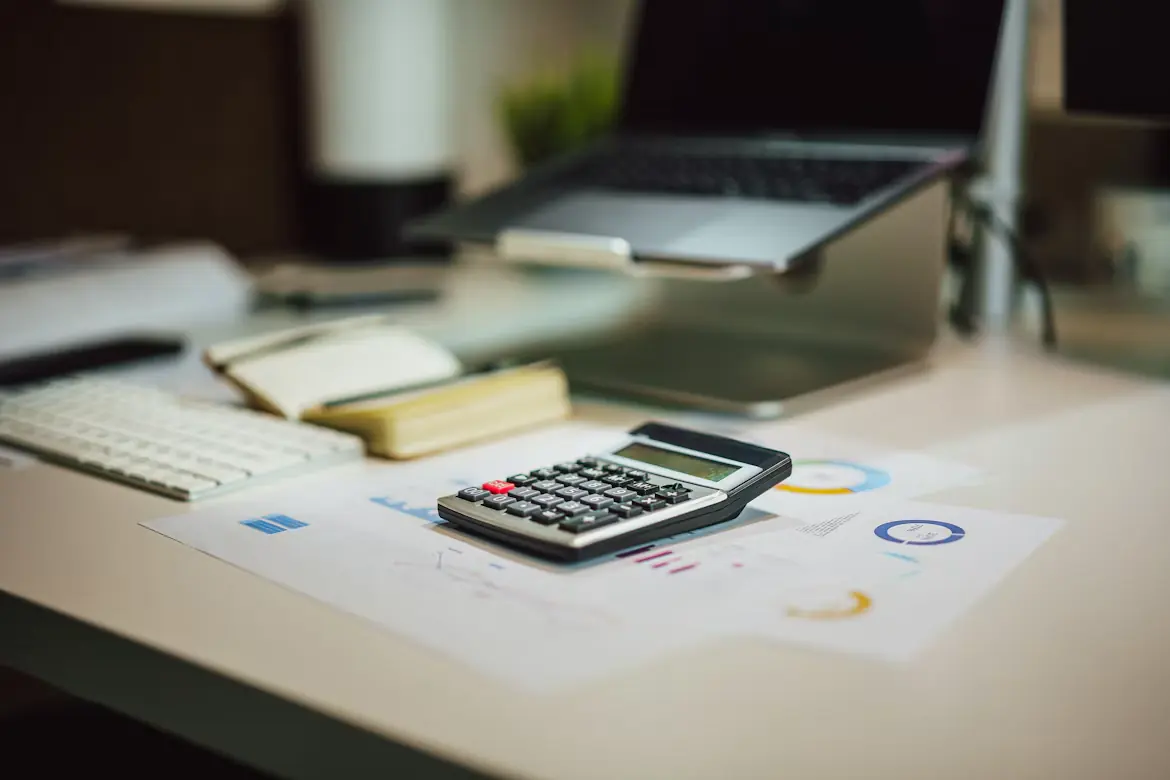 A desk with a laptop, a calculator and documents with charts