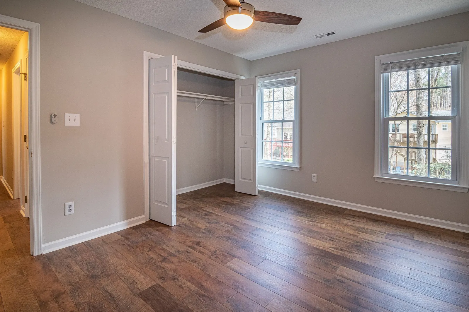 An empty room with wood floors, an open closet and two windows