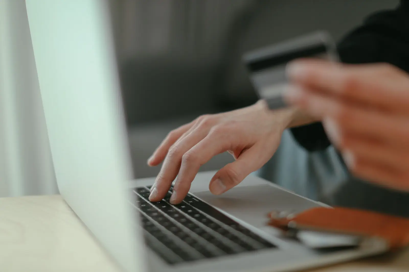 Una persona escribe en una laptop mientras sostiene una tarjeta en la otra mano