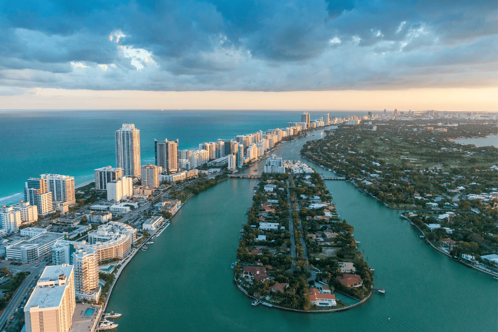 Aerial view of Miami Beach at dusk: oceanfront towers, the Indian Creek waterway and a residential island with homes among trees