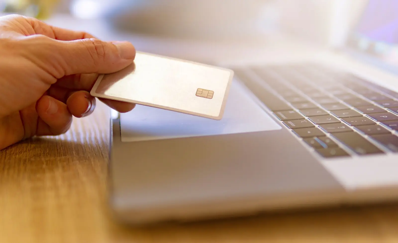 A hand holds a plain chip card next to a laptop keyboard