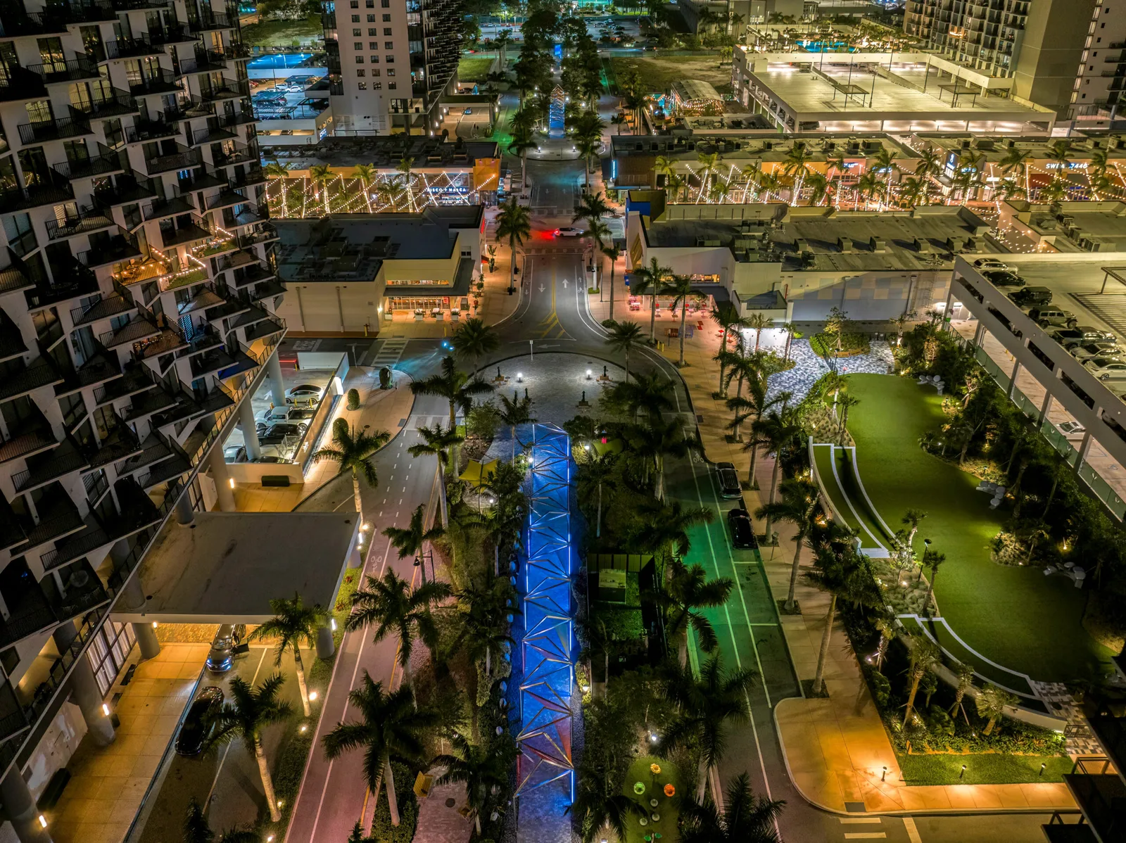 Night aerial view of downtown Doral, with apartment towers, a lit promenade with palm trees and restaurant terraces