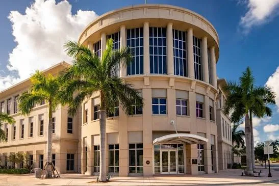 A cream-colored office building with a cylindrical glass tower and palm trees in front