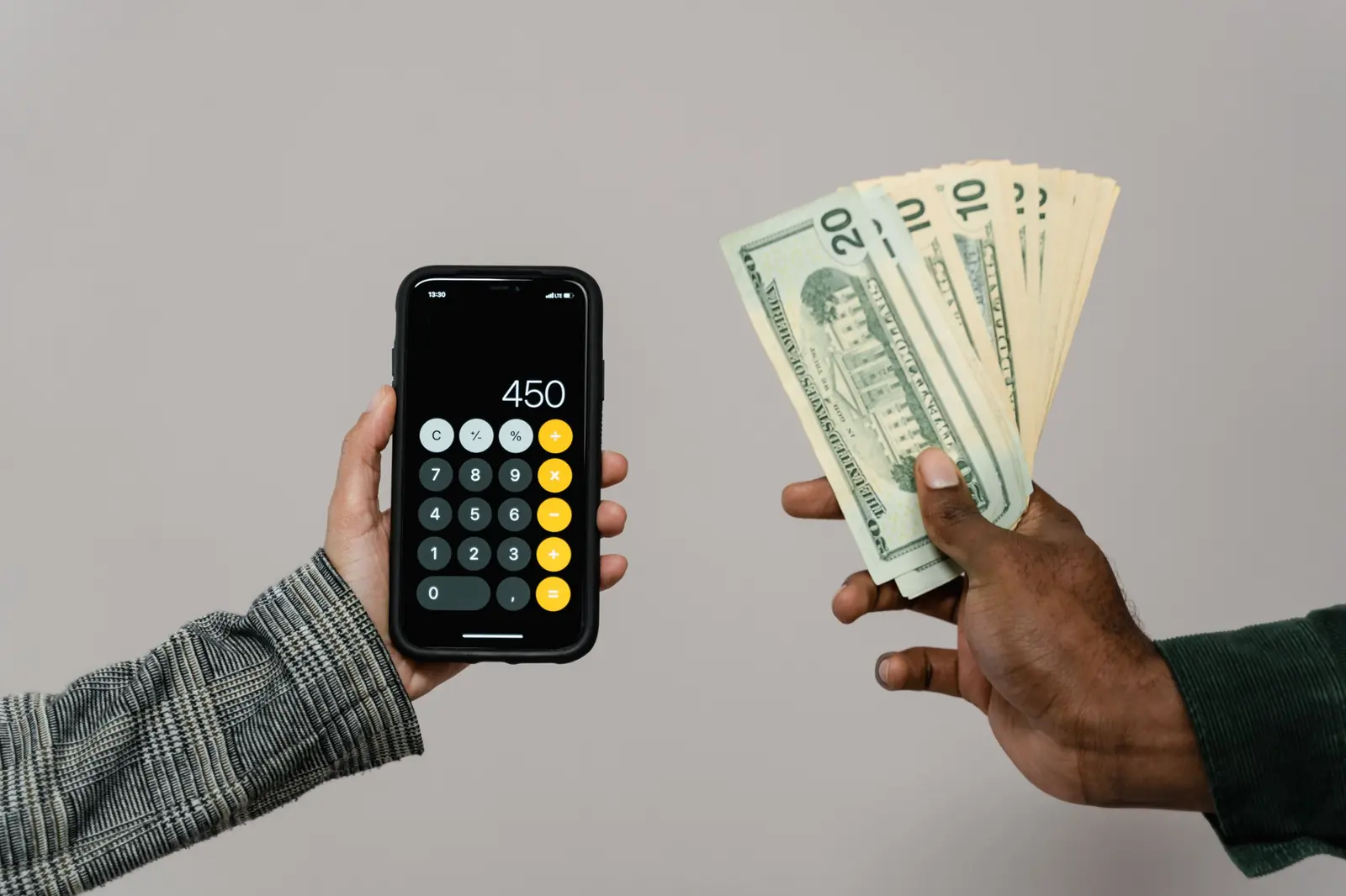 One hand holds a phone with the calculator open while another hand holds dollar bills