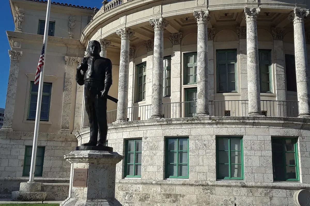Coral Gables City Hall, a stone building with columns and a clock tower, with a bronze statue in front