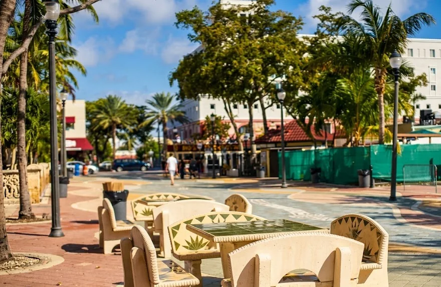 Stone tables and seats decorated with tiles on a pedestrian promenade with palm trees and street lamps, next to Calle Ocho