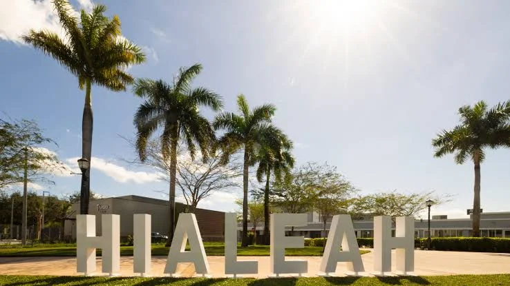 Large white letters spelling Hialeah on the lawn of a park with royal palms