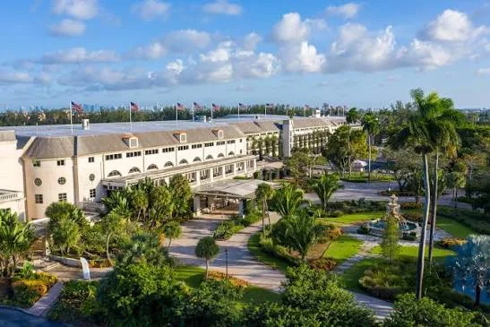 Aerial view of a large cream-colored building with flags, fountains and palm-lined gardens