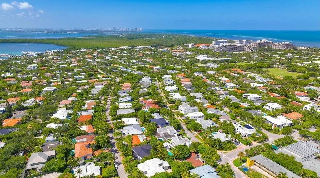 Aerial view of Key Biscayne residential streets, with homes among trees, oceanfront towers and downtown Miami in the distance