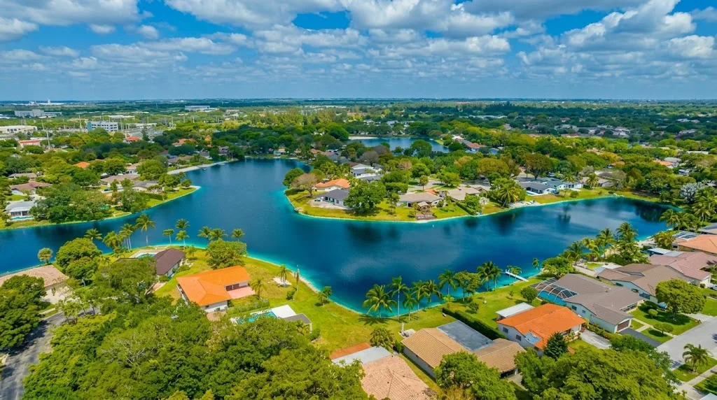 Aerial view of a blue lake surrounded by tile-roofed houses, palm trees and greenery