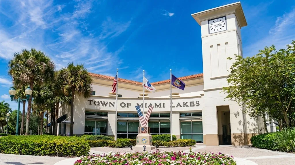 Miami Lakes town hall, a cream-colored building with a clock tower, flags and palm trees