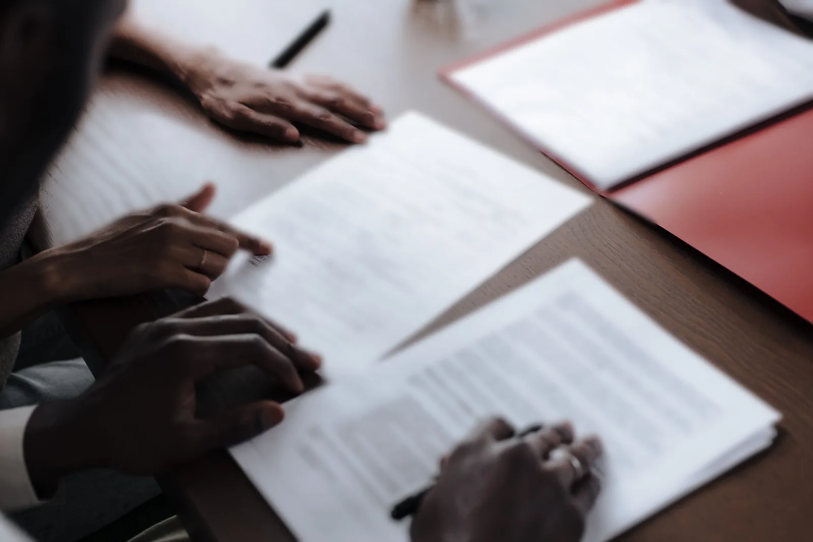 Hands over purchase documents on a wooden table, next to a red folder