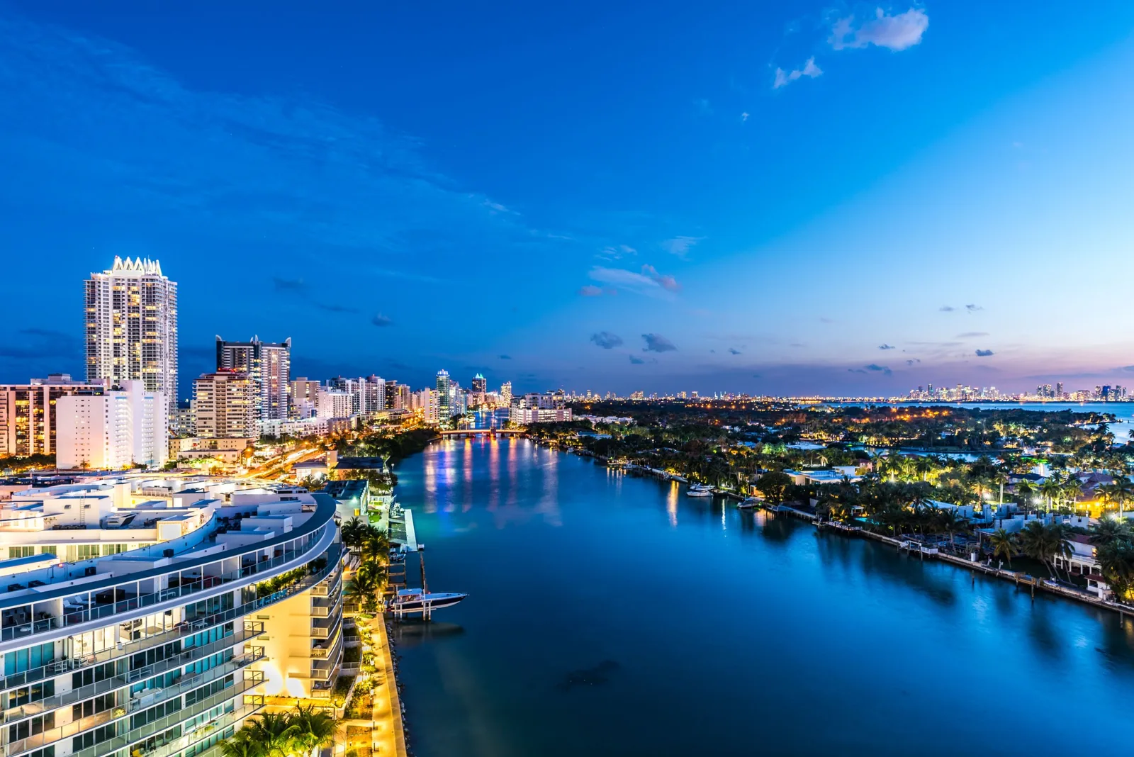 Waterfront homes on Indian Creek, Miami Beach, at dusk, with palm trees and moored boats