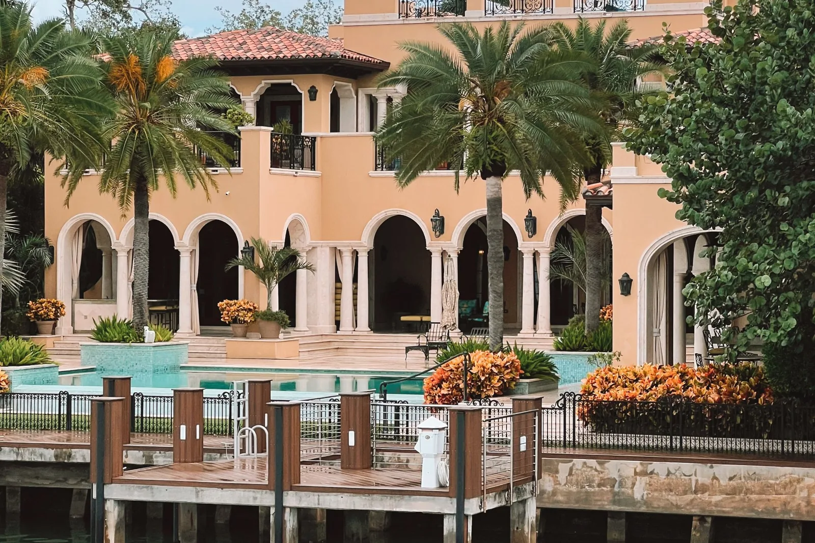 Mediterranean-style waterfront house with arches, palm trees, a pool and a wooden dock