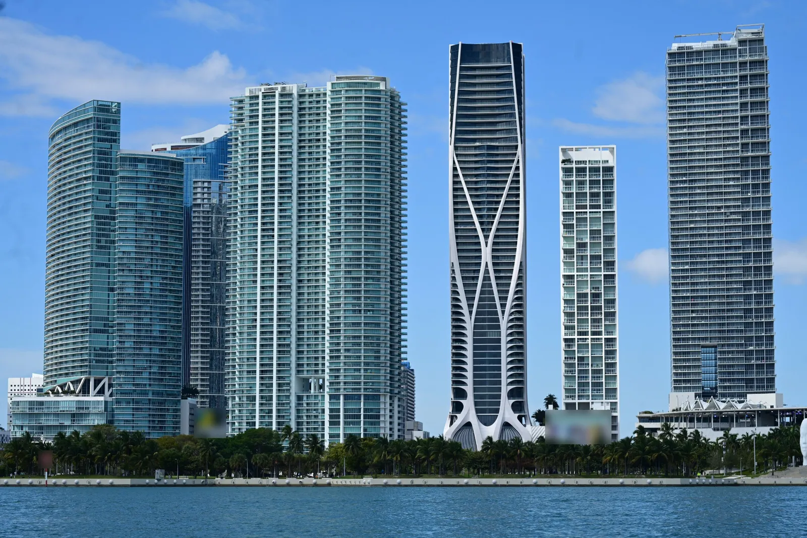 Residential towers in downtown Miami beside a palm-lined park, seen from Biscayne Bay