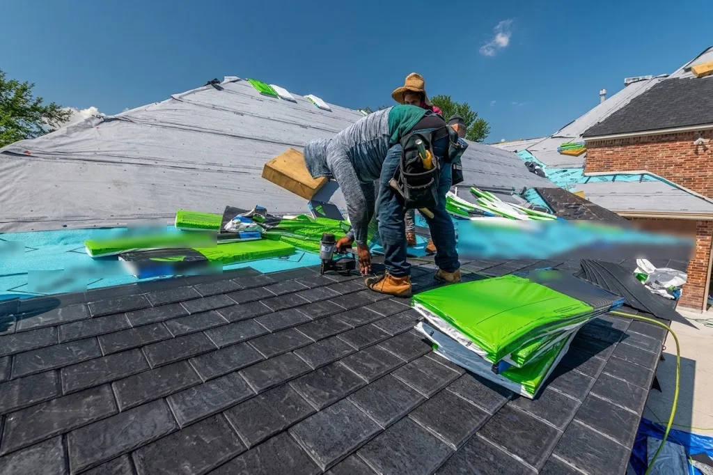 Two workers installing new shingles on a house roof over a waterproof underlayment