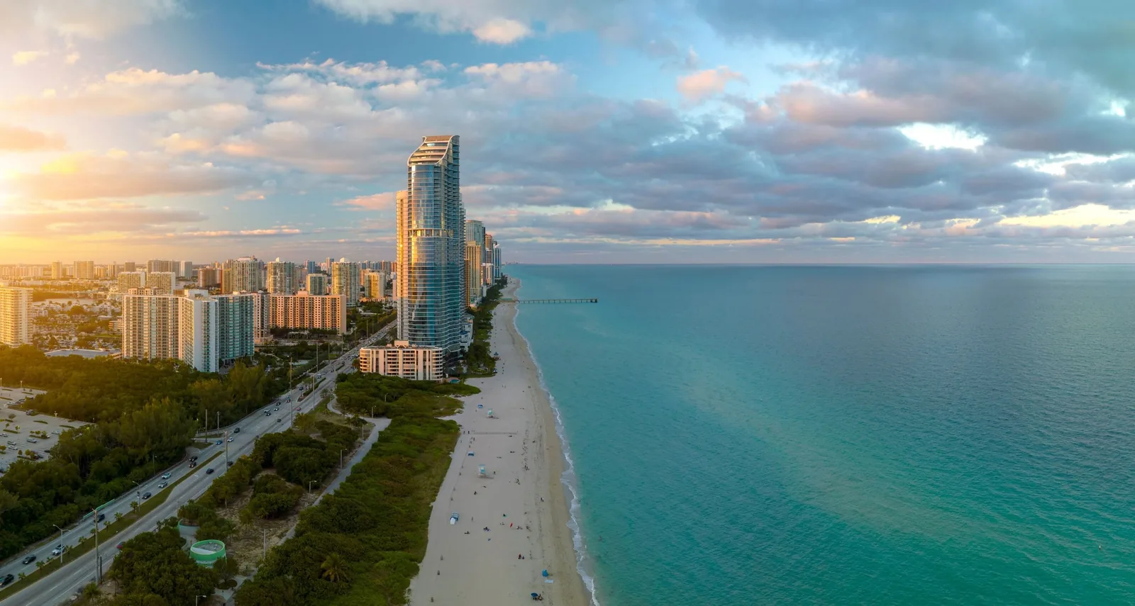 Aerial view of Sunny Isles Beach at sunset, with a glass tower, the fishing pier and turquoise water