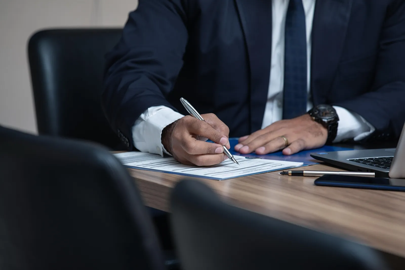 A person in a suit fills out a form with a fountain pen at a meeting table