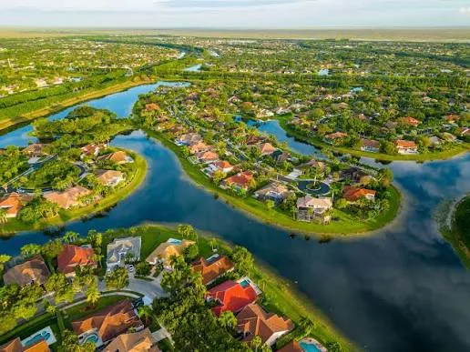Aerial view of a community of tile-roofed houses with pools around lakes and canals, with the Everglades in the background